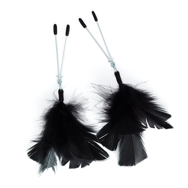 Close-up of black feather nipple clamps with metal clips, creating a boudoir aesthetic.