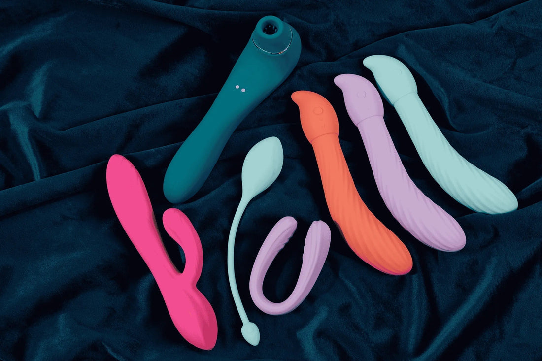 Buying your first vibrator - Image of 7 different types of colourful vibrator on a dark green background.