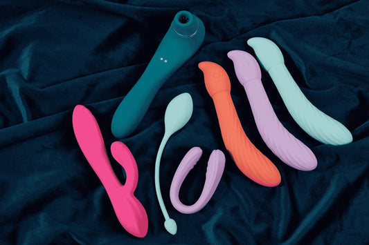 Buying your first vibrator - Image of 7 different types of colourful vibrator on a dark green background.